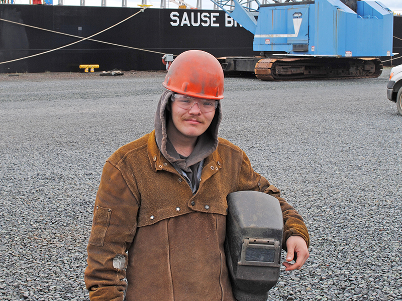 Photo of young man in welding gear standing in front of a cargo ship