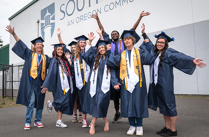 a group of young people dressed in graduation robes and caps holding their arms out