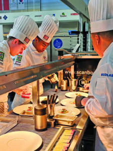 image of three chefs working in a commercial kitchen with plates on a counter in front of them