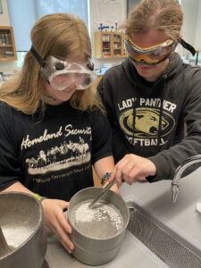 two young women working at a work bench crushing oyster shells