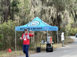 Image of Clackamas Community College President, Dr. Tim Cook, on an outdoor run with trees in background and a water station with a canopy that reads "run for a reason" 