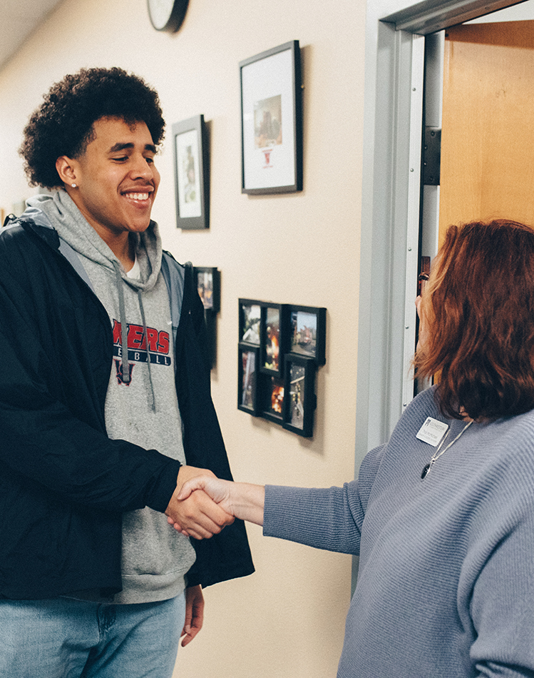 Advising webpage-Trish and student image of a young man shaking hands with a woman in front of an office door