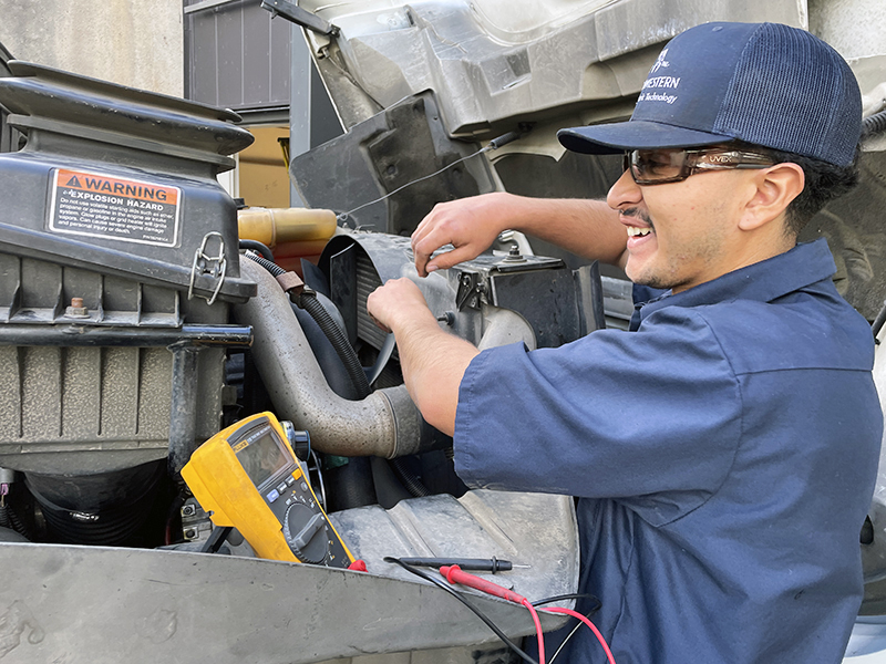 a diesel mechanic student smiles while working on a motor