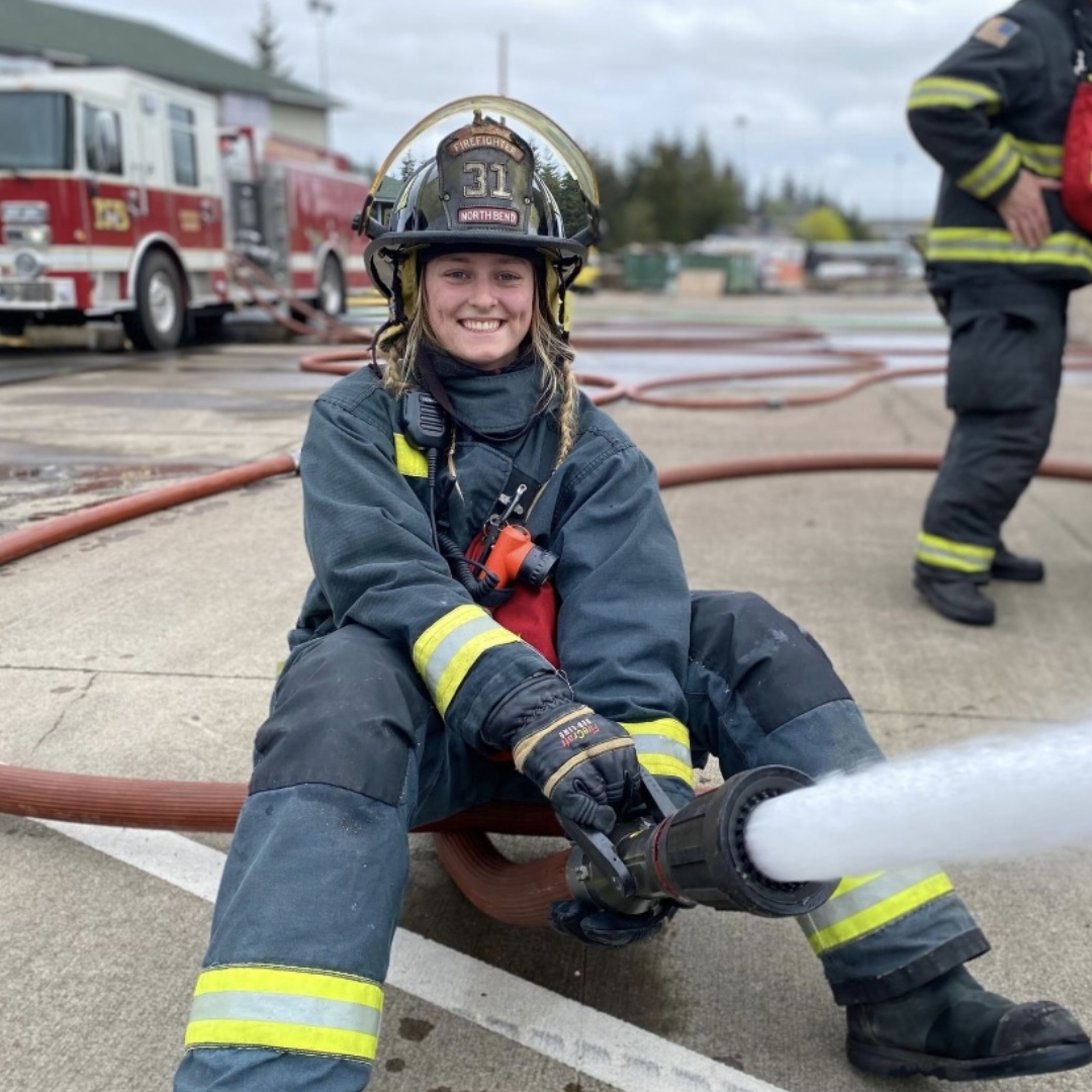 Image of Fire Science graduate Kimber Privetts sitting on concrete holding a fire hose