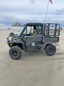 Image is of a woman driving a 4-wheel drive vehicle on the beach, with the ocean in the background