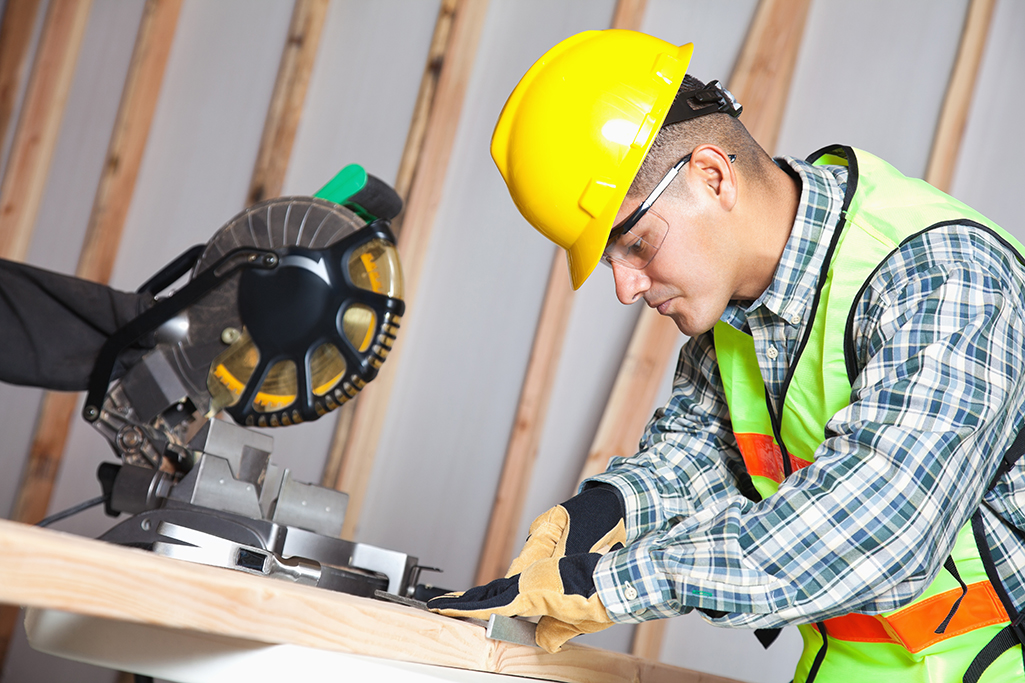 Construction worker measuring wood with miter saw at work site Image of a heavy equipment operator in a hard hat measuring wood with a circular saw in the background