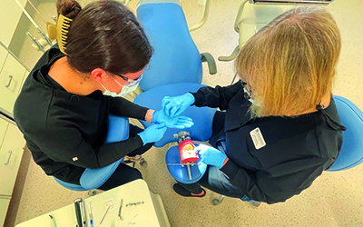 Image is above the heads of two women, one is a dentist, the other is the assistant and she is holding out her hand for the dentist