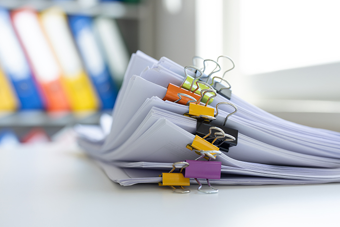 Image of a stack of papers with divided up with colored clips sitting on a desk, with a cabinet in the background