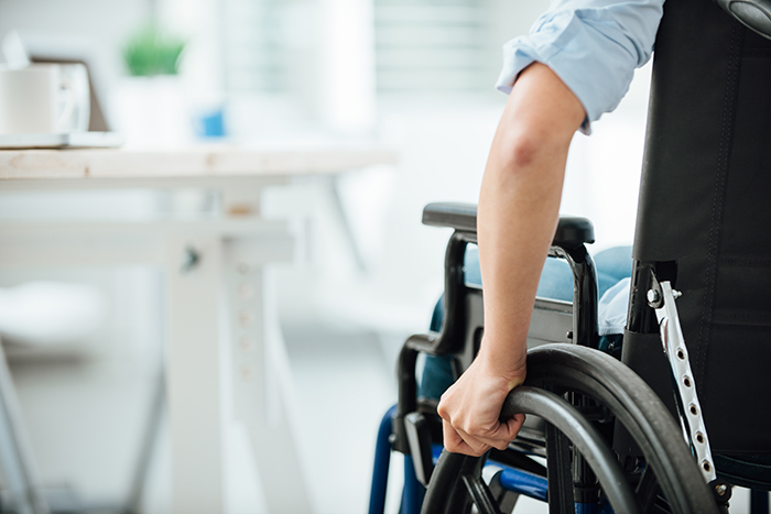 Image is a back view of a person in a wheel chair with hand on wheel. Table in chairs in background.