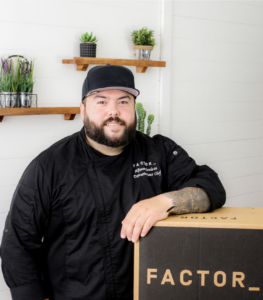 Portrait of Chef Alfonso Mendoza standing with arm on top of a Factor box