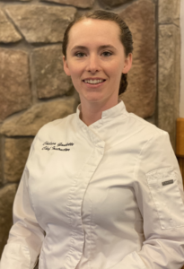 Portrait of Chef Chelsea Gaudette standing indoors in front of a rock wall background