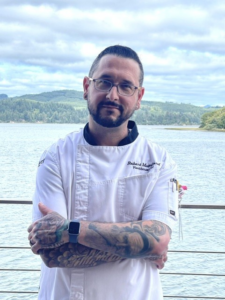 Portrait of Chef Bryan Elam standing outdoors with his arms crossed and a bay view in the background