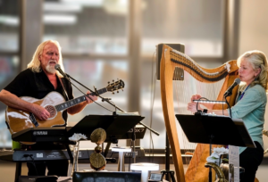 Image of the Uncorked Duo - one playing a guitar and the other playing a harp