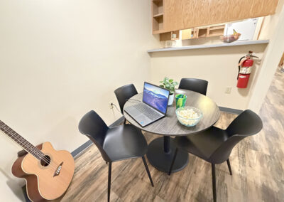 image of the dining area showing the dining table, four chairs, laptop, bowl of popcorn, drink glass, plant, guitar in the corner on the floor, looking across to the bar that passes into the kitchen area