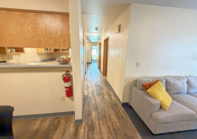 image is the apartment hallway where you can see the corner of the couch, the bar going into the kitchen, and down the hall to the bedrooms