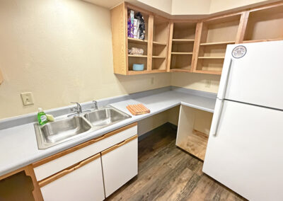 image of the kitchen area of an apartment showing the sink, countertops, cupboards, and refrigerator