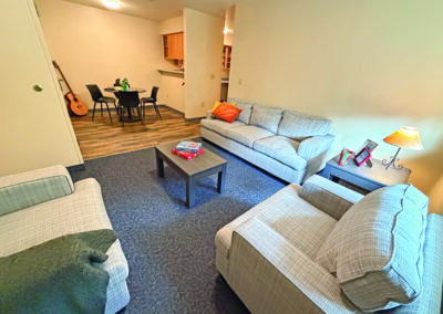 image of the living room with couch, two chairs, two coffee tables, looking across the room into the dining area