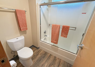 image of bathroom with bathtub and shower and toilet, there are orange colored towels on the towel racks